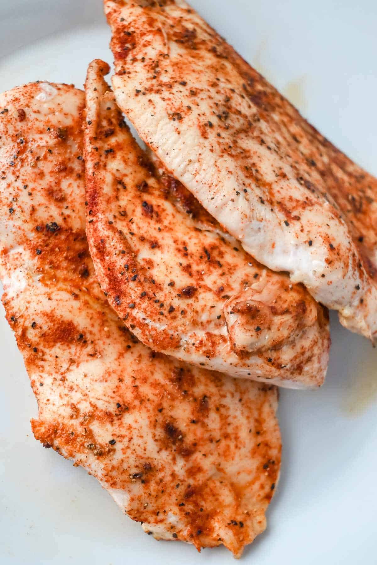 cooked and seasoned thinly sliced chicken breast on a white plate.