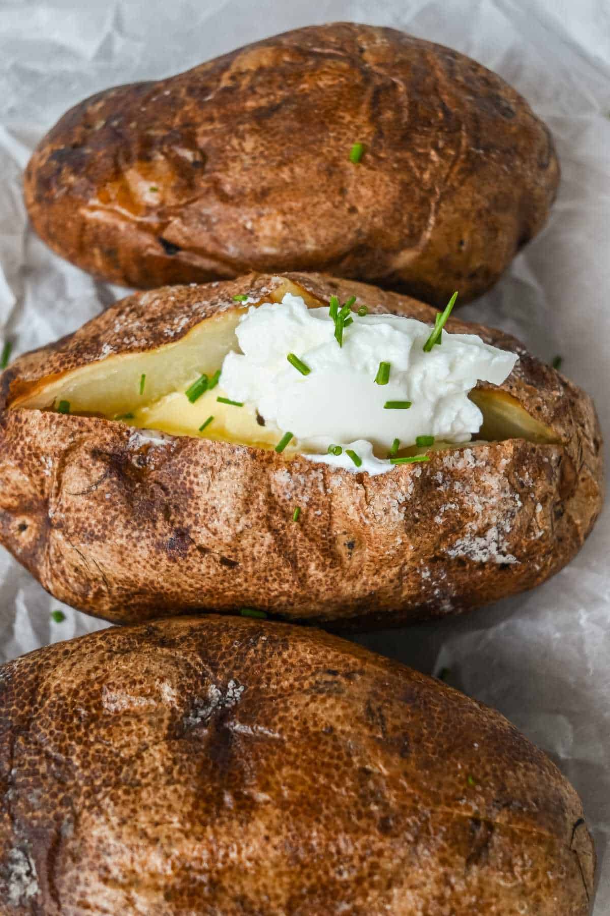 three cooked potatoes with one topped with sour cream, butter, and chives.