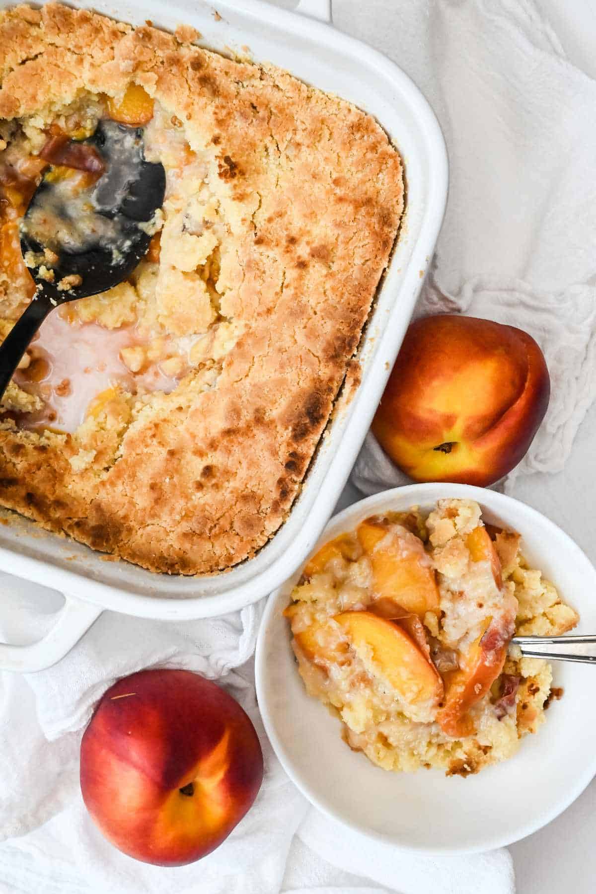 full pan of peach cobbler with a spoon next to a bowl of peach cobbler.