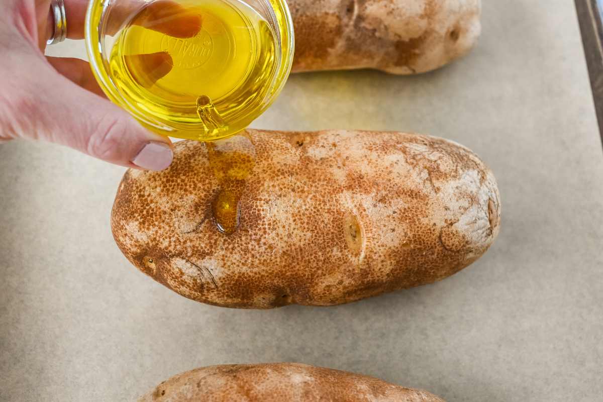 hand drizzling olive oil over potato skin.