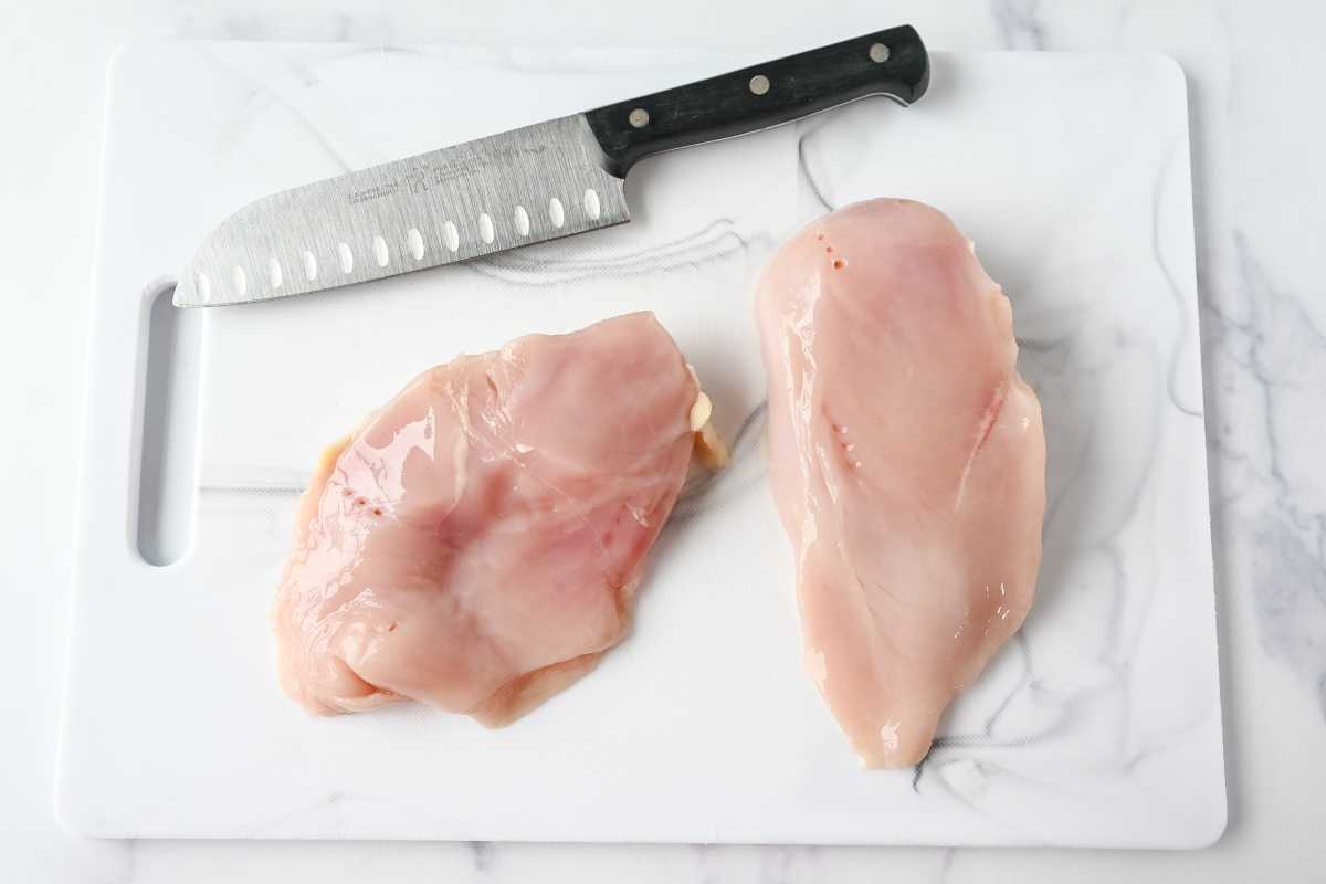 raw chicken on a white cutting board with a knife.