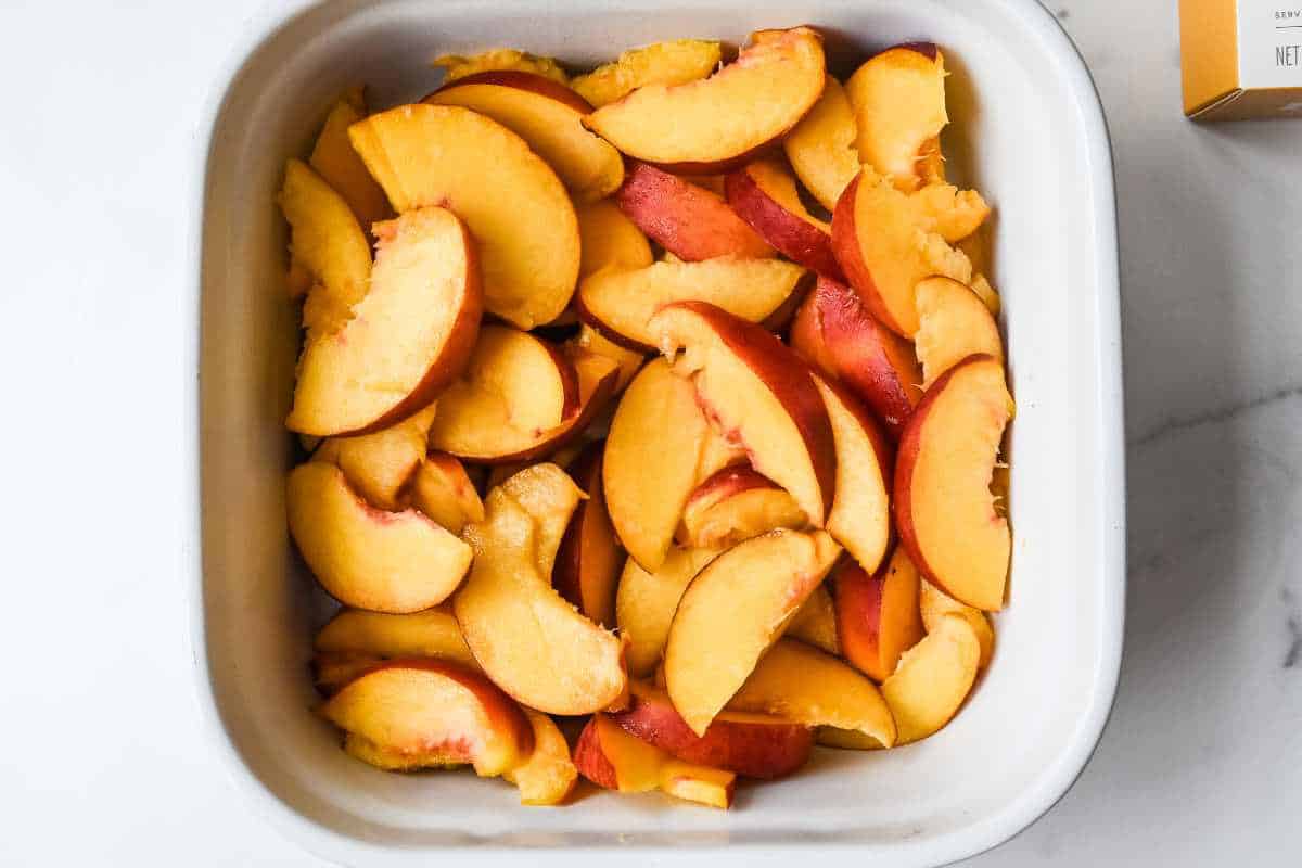 sliced fresh peaches in a white baking dish.
