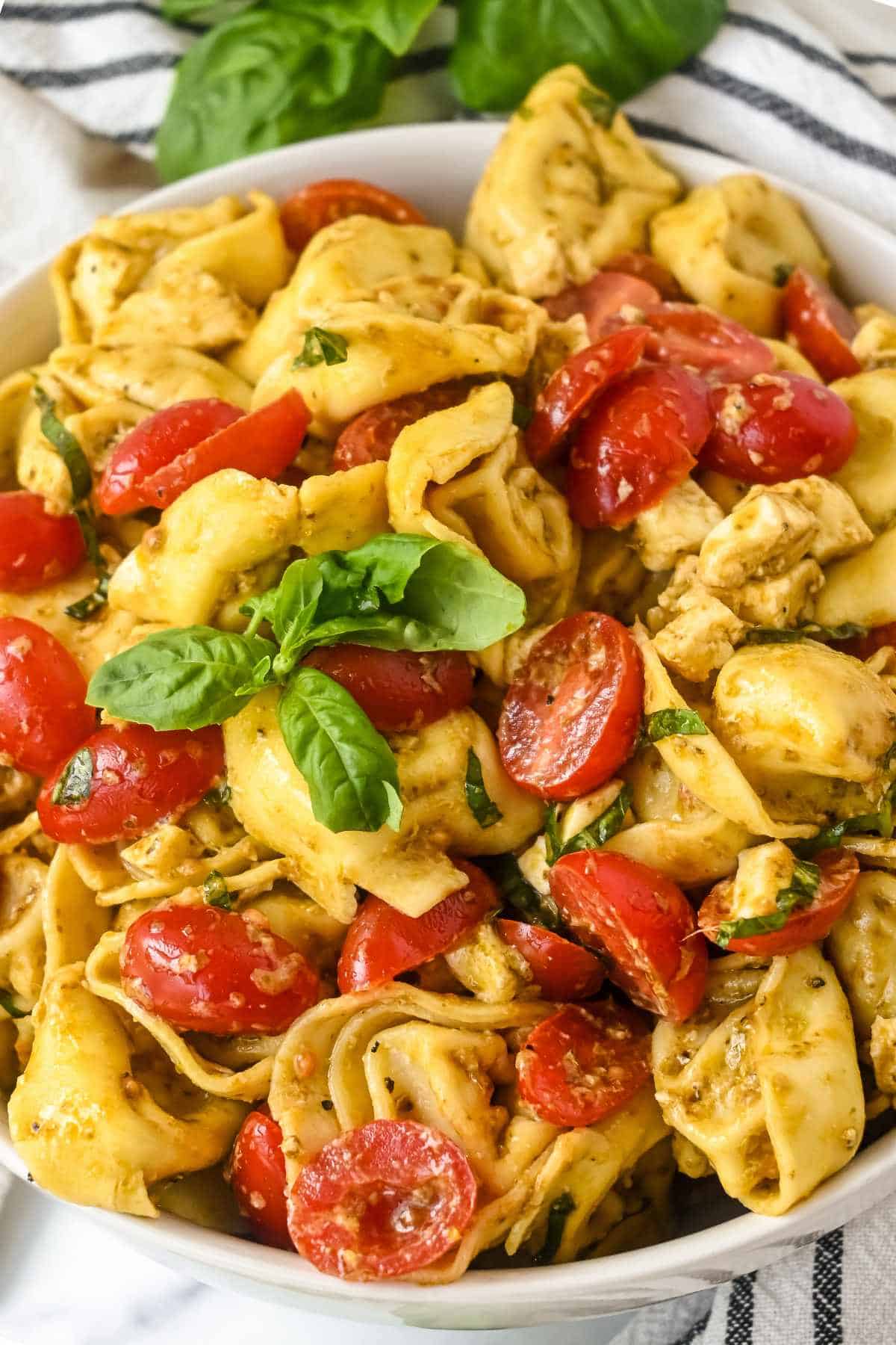 full bowl of pesto tortellini salad with tomatoes and basil.