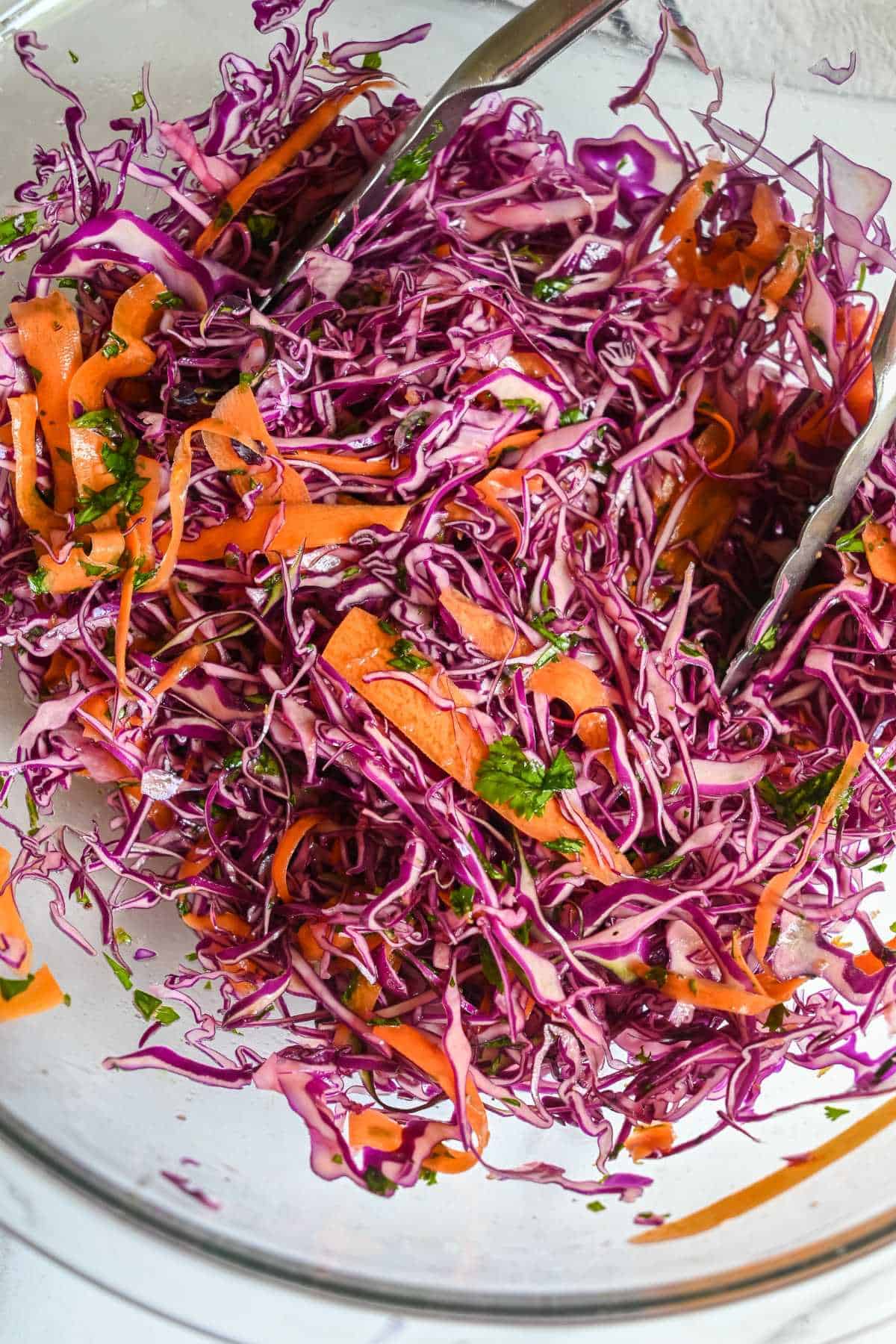 red cabbage slaw in a glass bowl with tongs.