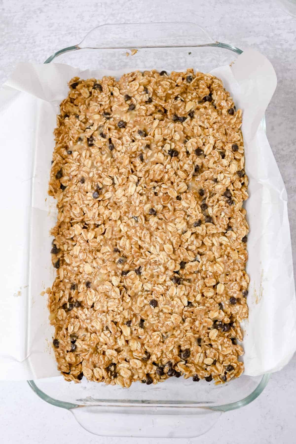 unbaked banana oatmeal bars in a glass pan with parchment paper.