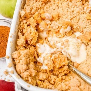close up of apple cobbler with cake mix in a white dish topped with ice cream and a spoon in the dish.