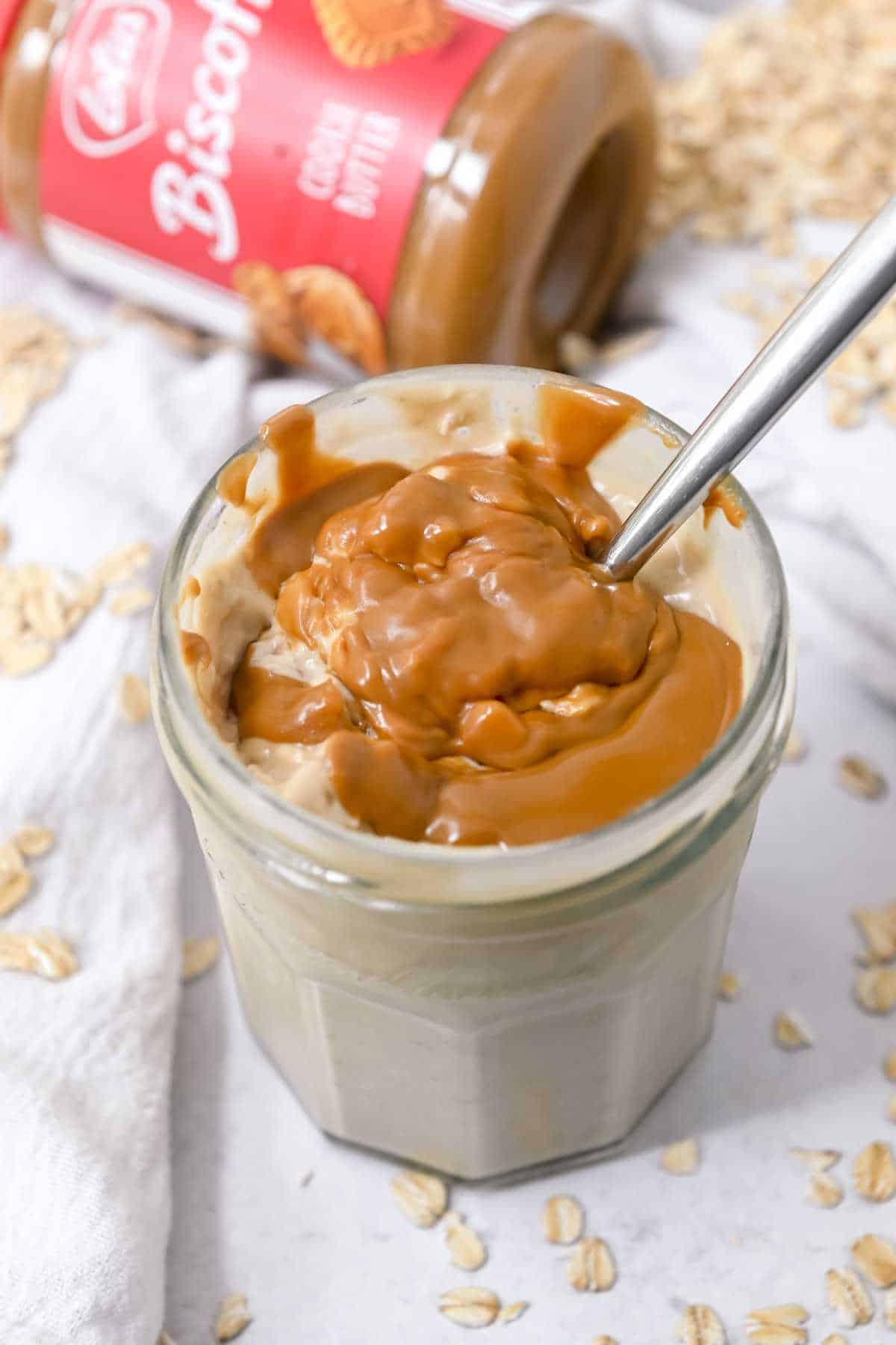 top down view of a jar of biscoff overnight oats on a white background with Biscoff and oats behind it.