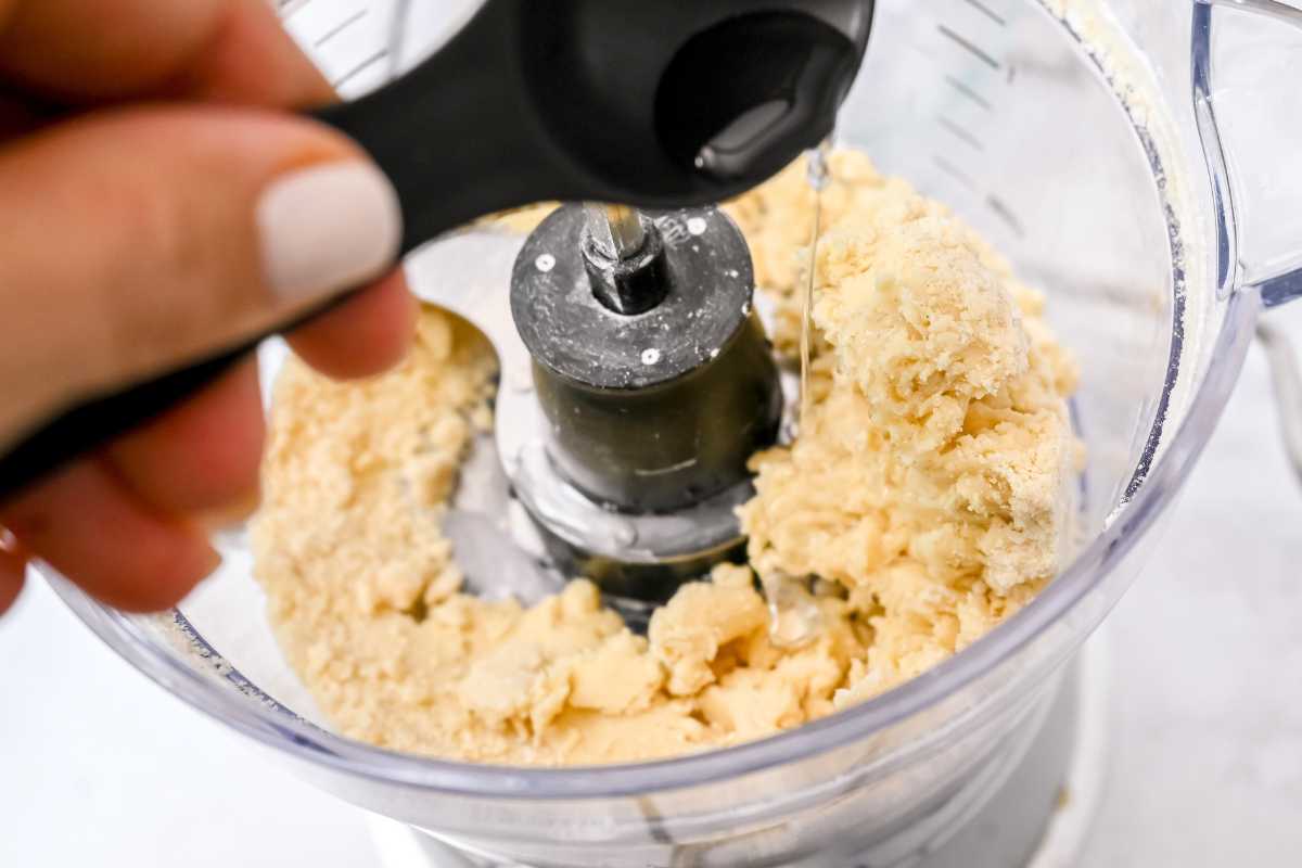 hand adding water to pie crust dough in a food processor.