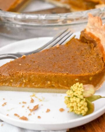 slice of eggless pumpkin pie on a white plate with a yellow flower next it.
