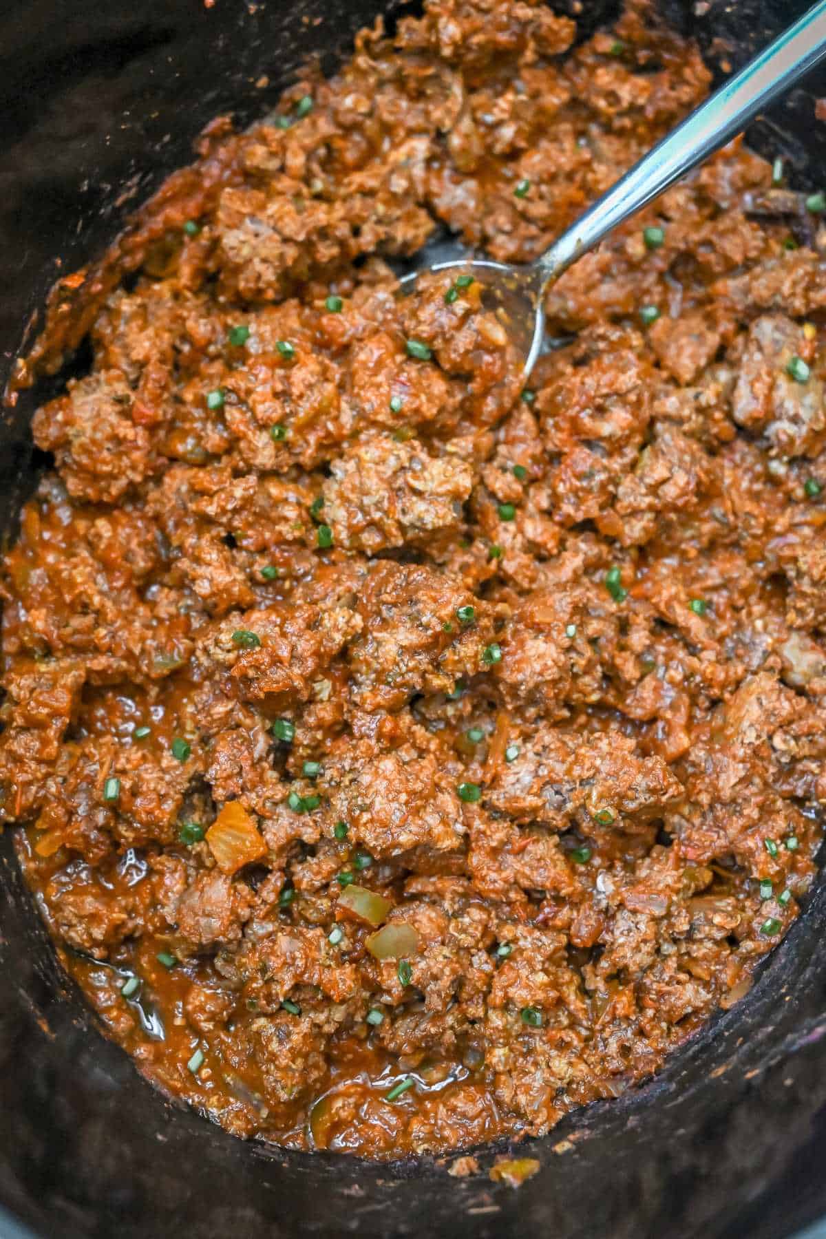cooked crockpot ground beef in a crock with a spoon.