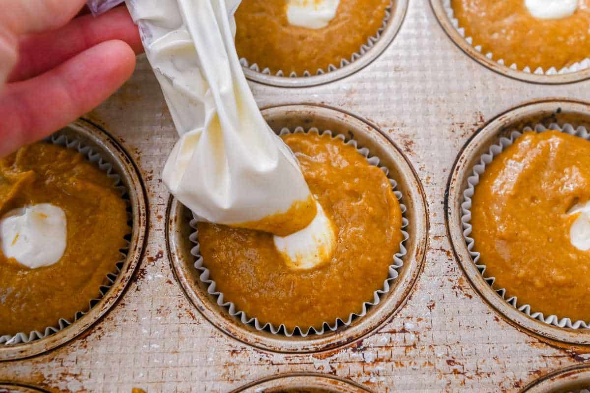 hand filling starbucks pumpkin muffins with cream cheese filling.