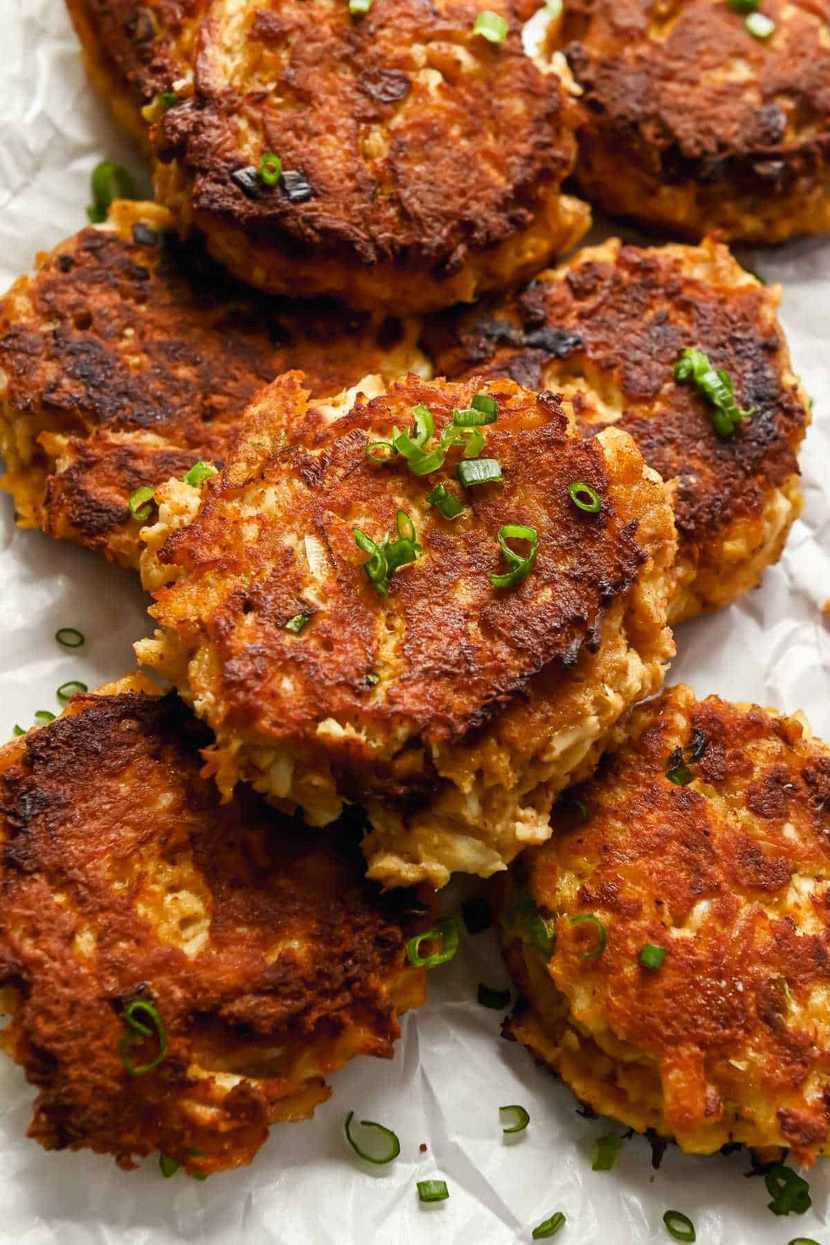 close up of maryland style crab cakes in a pile topped with green onions.