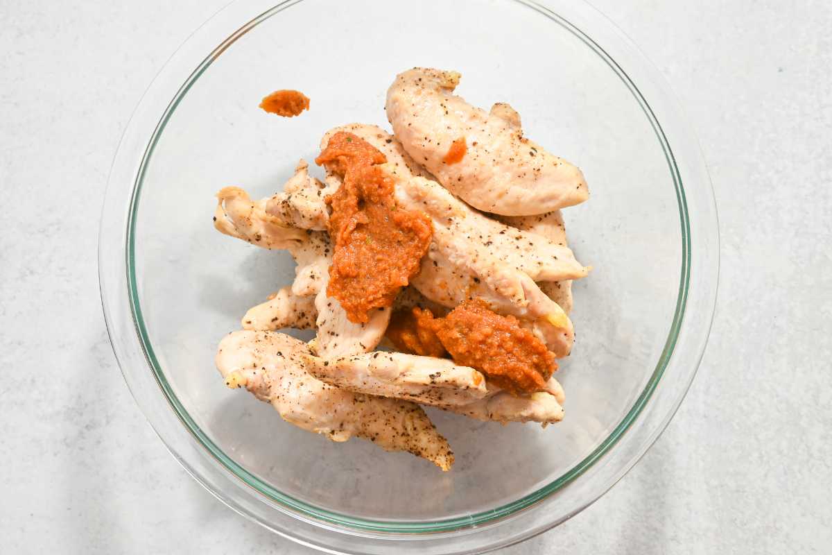 cooked chicken tenders in a glass dish with homemade buffalo chicken sauce on top.