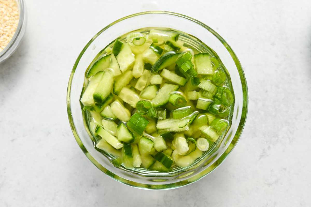 green onions and cucumbers in vinegar in a glass dish.